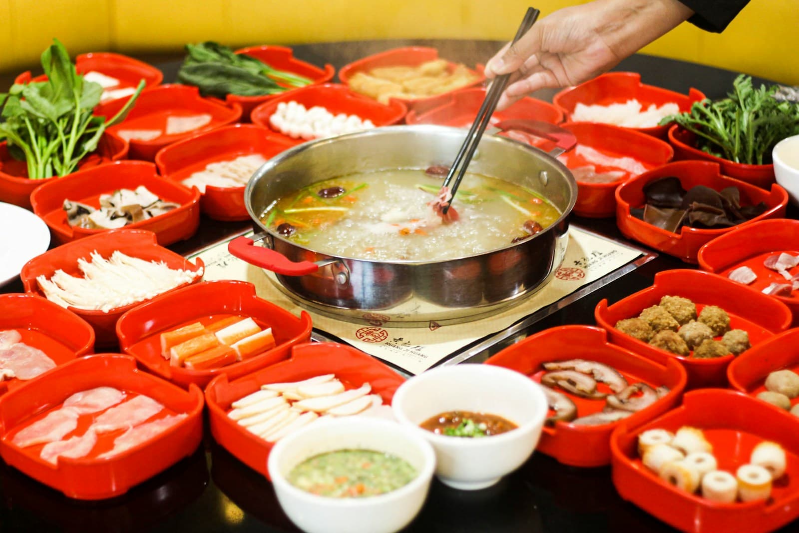 A Sichuan hotpot meal surrounded by colorful plates of fresh ingredients